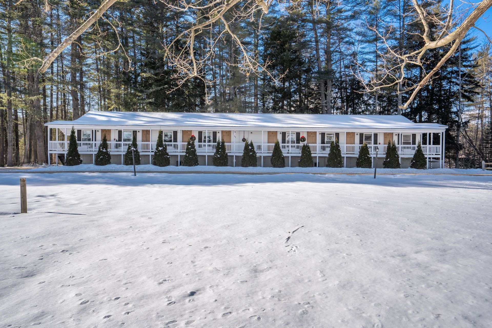 A long, white motel building in a snowy field, with evergreen trees in front of the building and behind it.