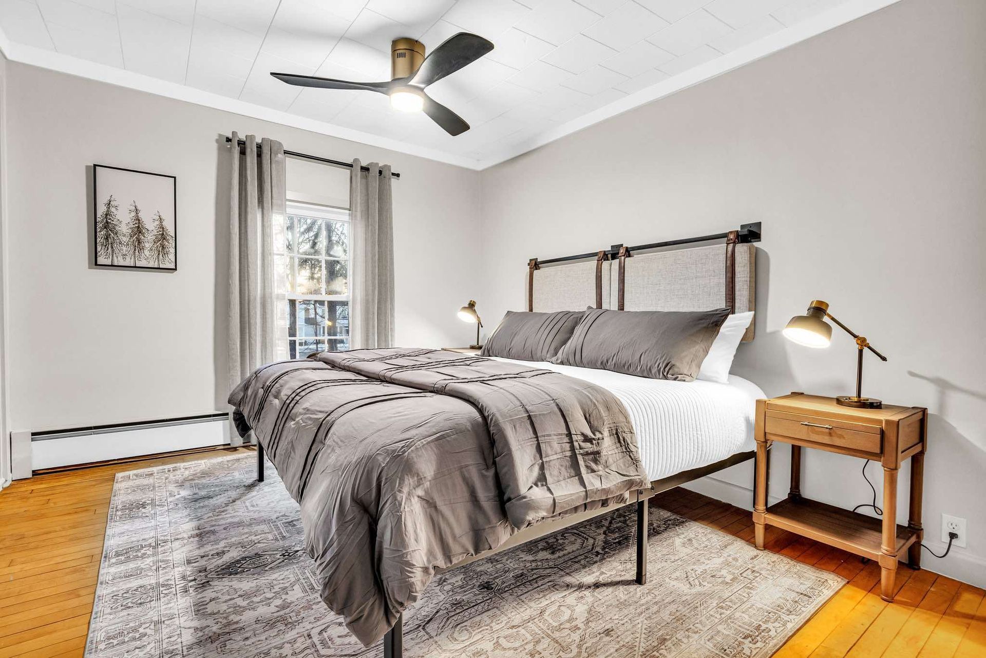 Bedroom with gray bedding, wooden nightstand, and framed art.