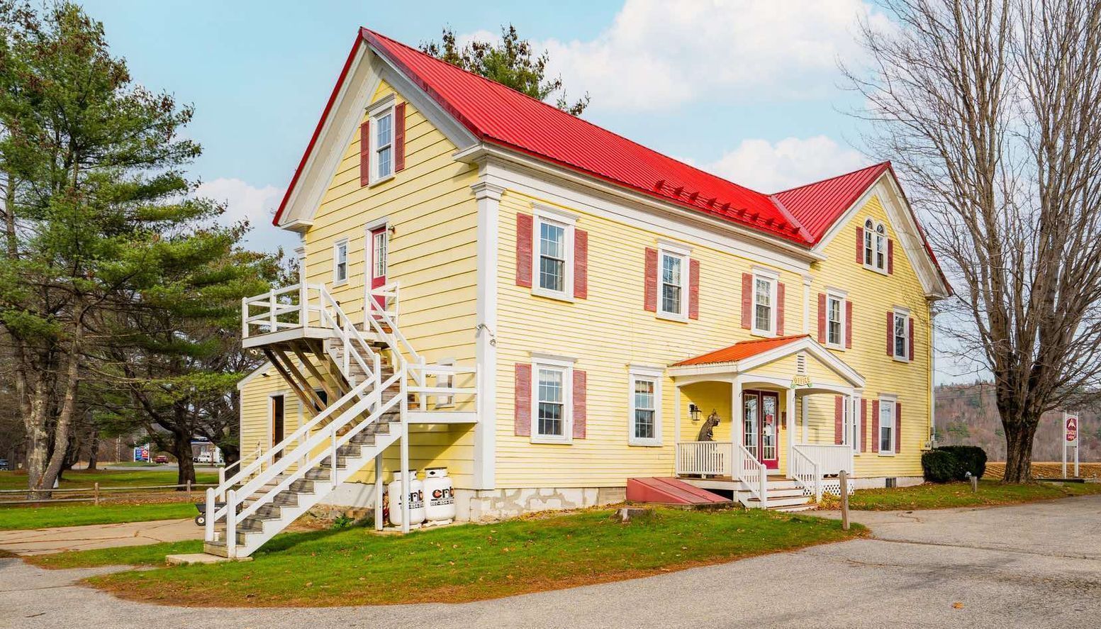 Yellow building with red roof and shutters, white stairs leading up to a balcony, and a porch entrance.