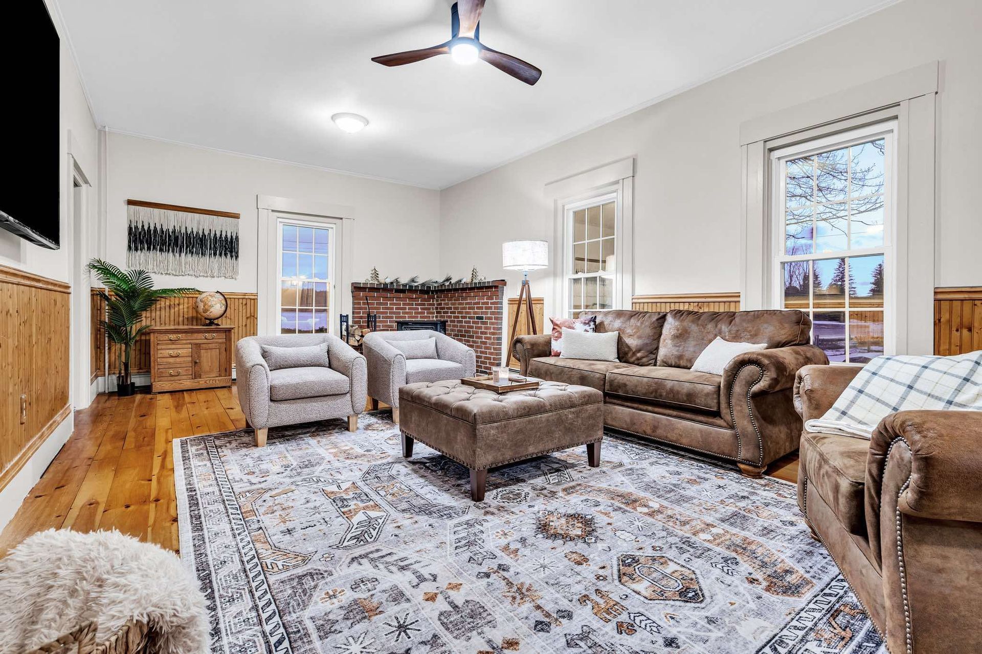 Living room with brown sofa, two armchairs, area rug, and wood paneling.