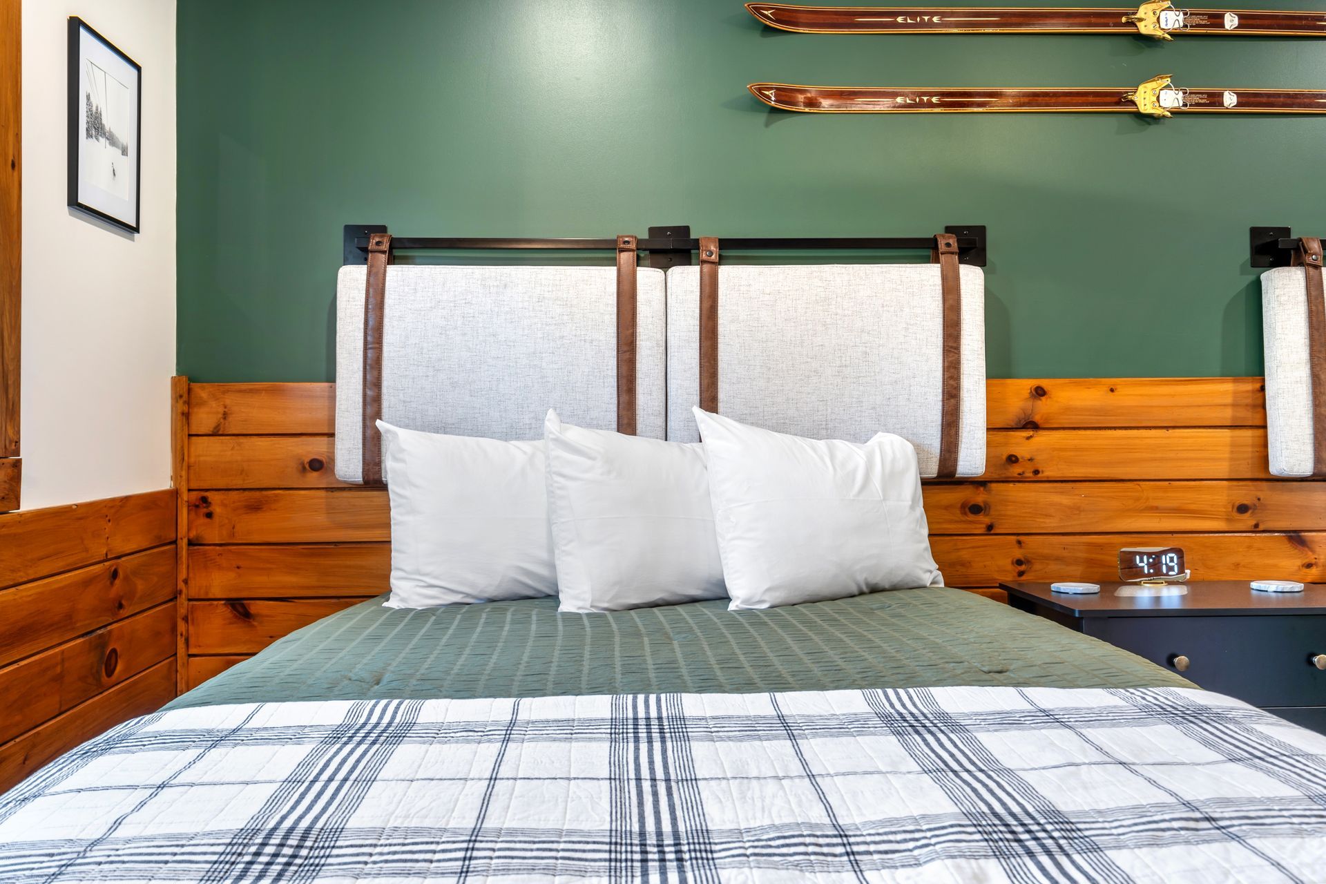 Bedroom with plaid bedspread, white pillows, wood paneling, and green accent wall.
