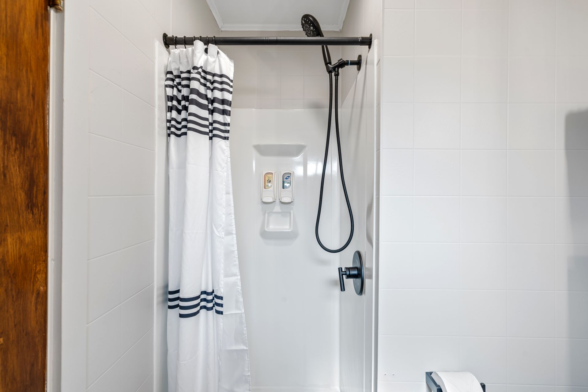 White shower with black fixtures and striped curtain.