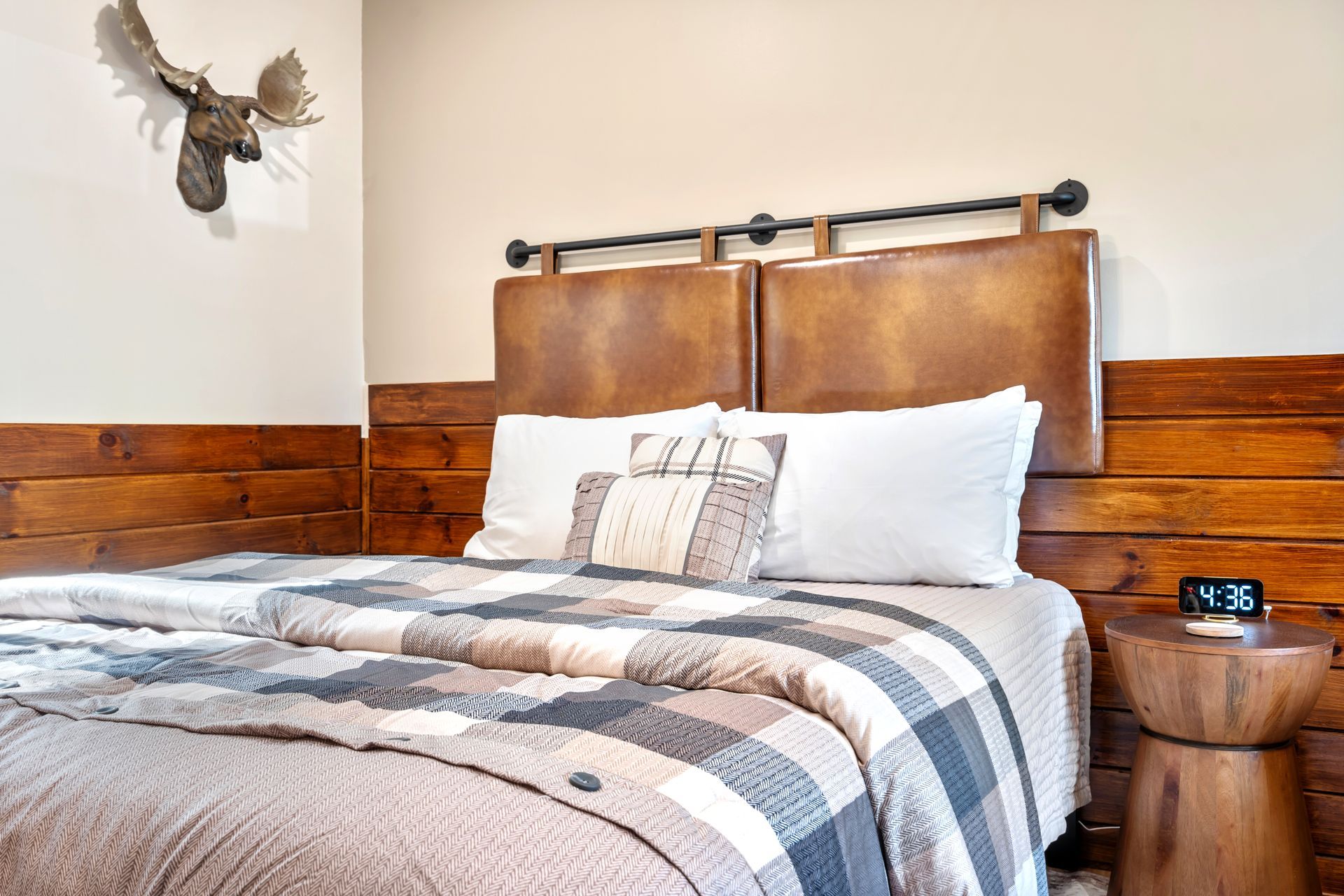 Bedroom with brown wood paneling, leather headboard, plaid quilt, side table, and moose head.