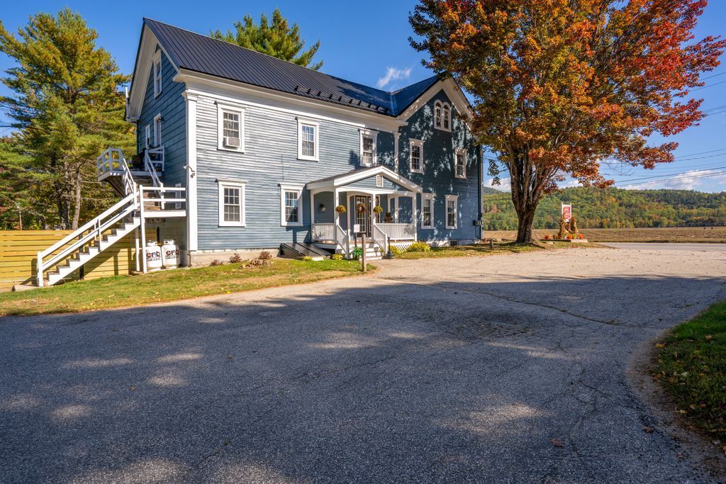 Yellow building with red roof and shutters, white stairs leading up to a balcony, and a porch entrance.