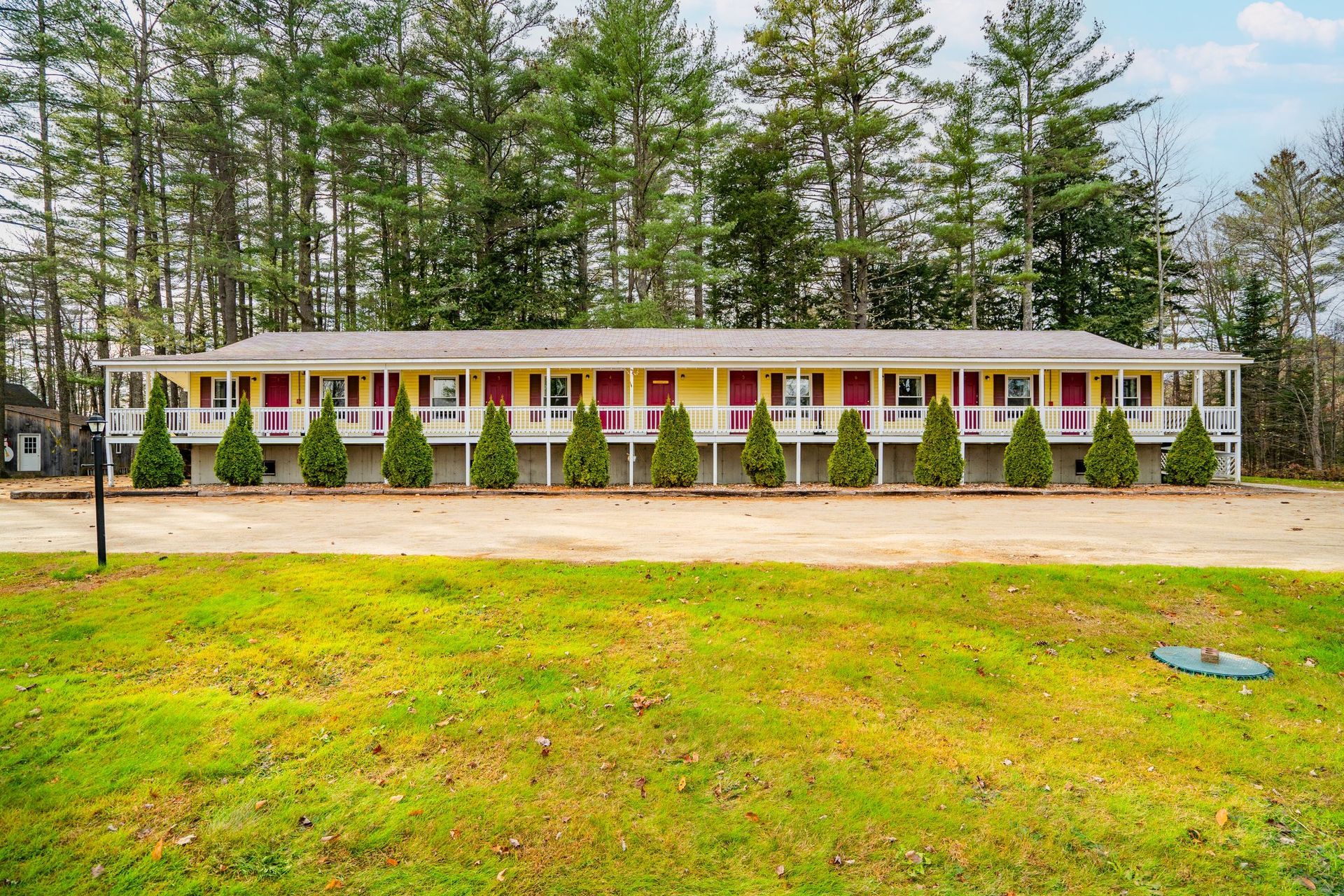 A one-story motel with yellow walls, red doors, and a long porch. Trees in the background.