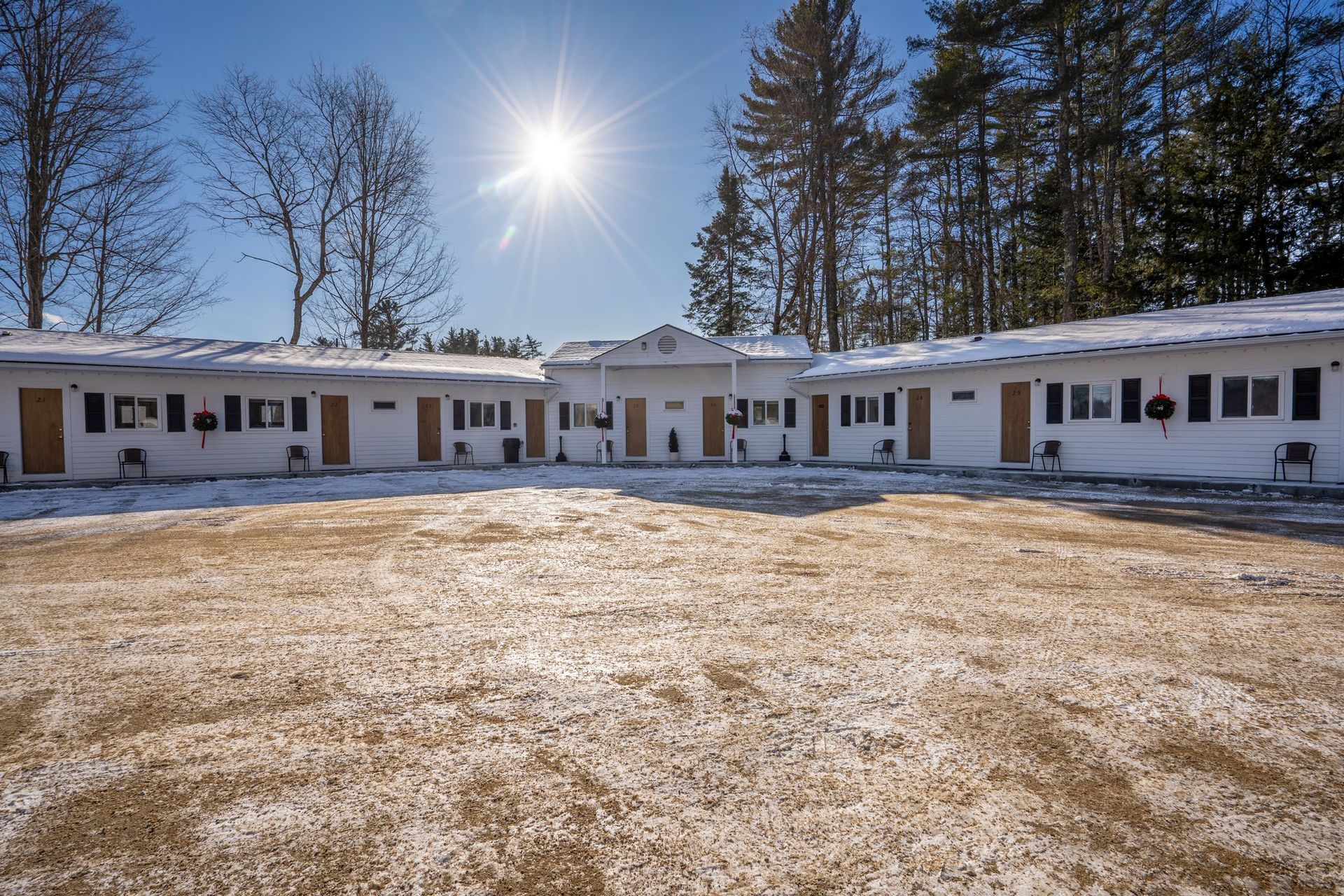Exterior view of a motel with white buildings, snow on the ground, and a bright sun in the sky.