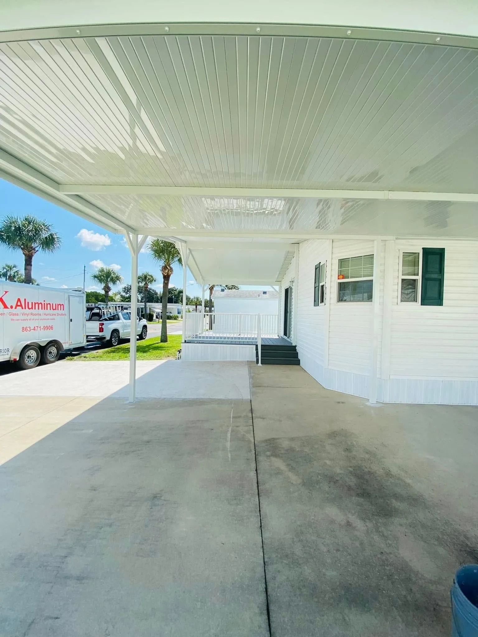 Covered concrete walkway beside a white building, with a parked truck and blue sky in the background.
