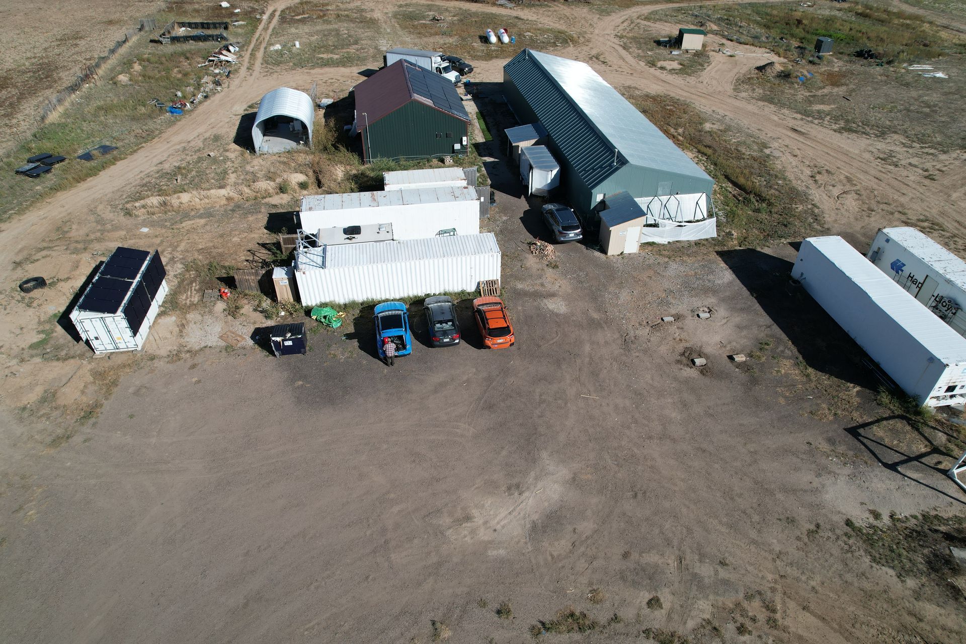 Aerial view of a The farm with buildings, trailers, vehicles, and solar panels.
