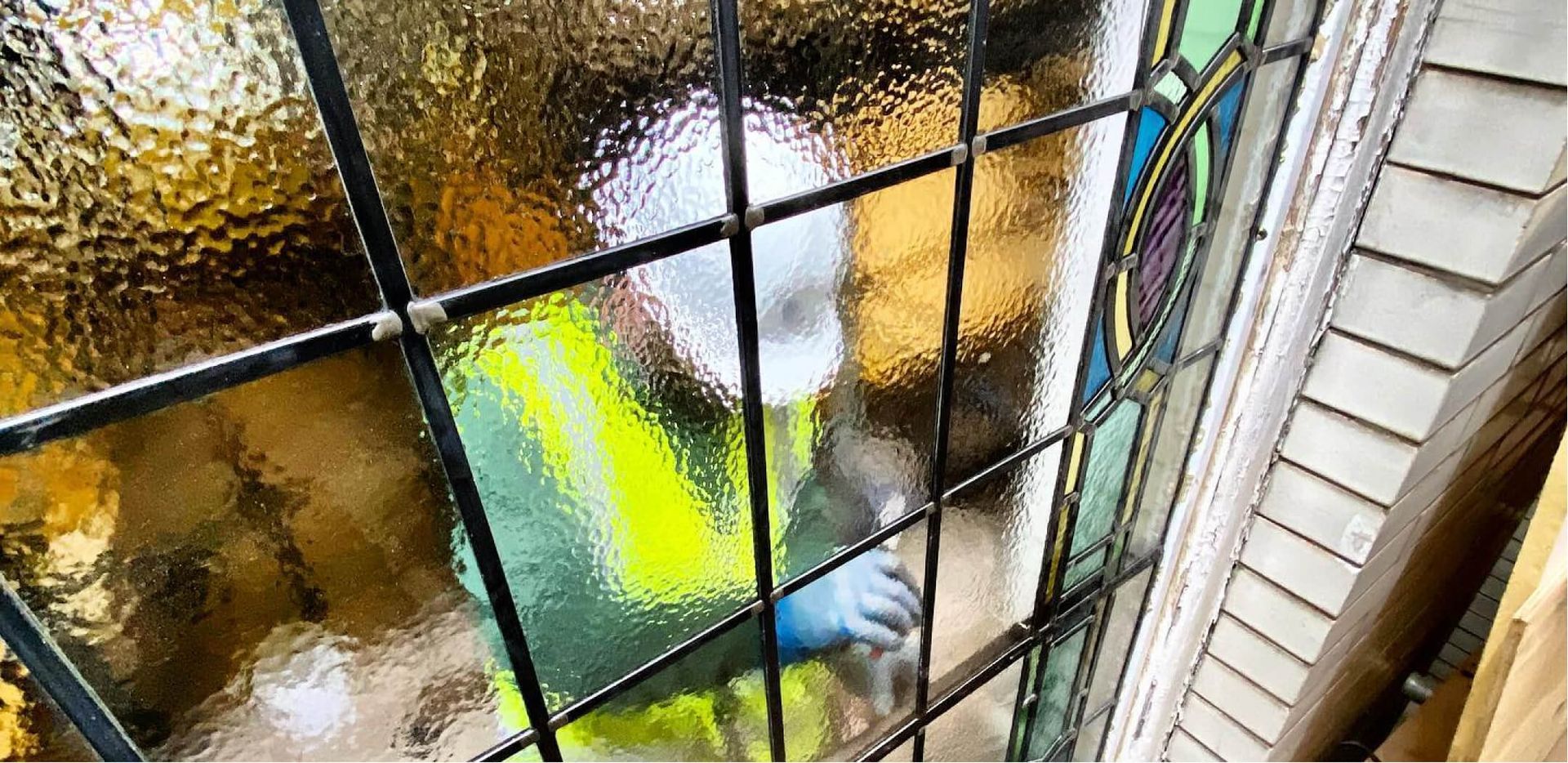 Person wearing a high-vis vest cleaning a stained glass window, seen through the window.
