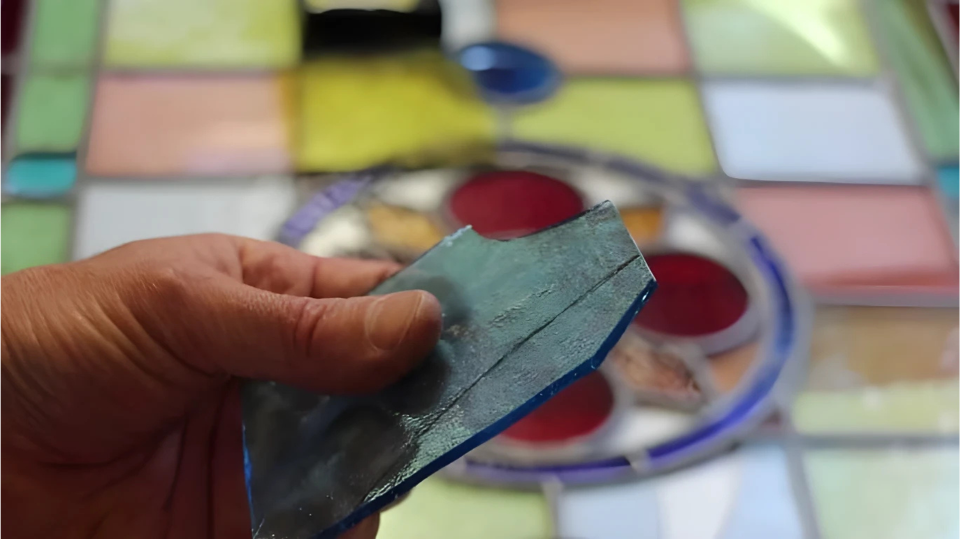 Person's hands working on a stained glass window. Colorful glass pieces, focused work setting.