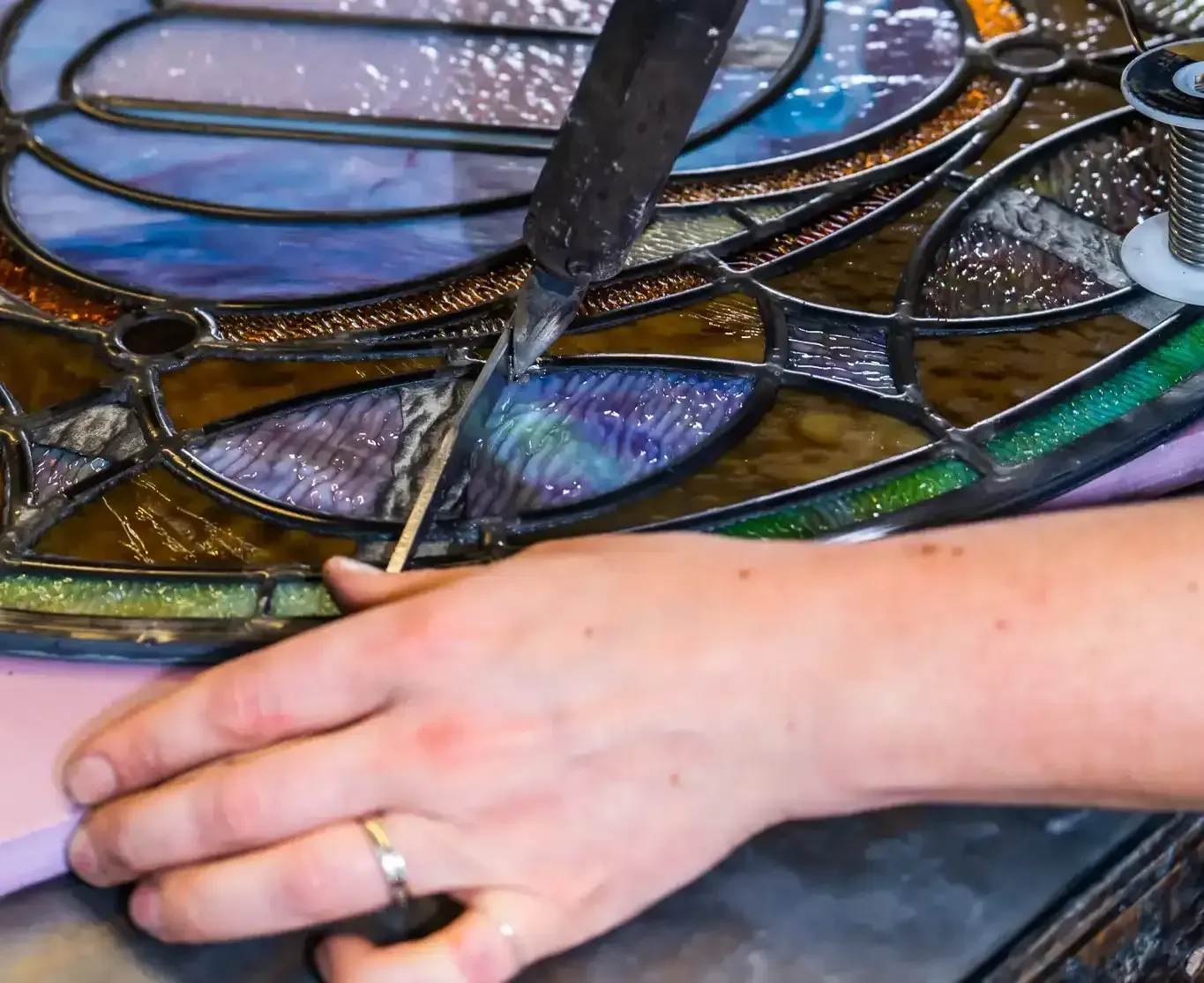 A group of people looking at stained glass on a lit table. Workshop setting, daylight.