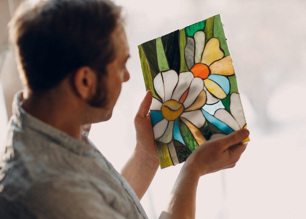 Person wearing a high-vis vest cleaning a stained glass window, seen through the window.