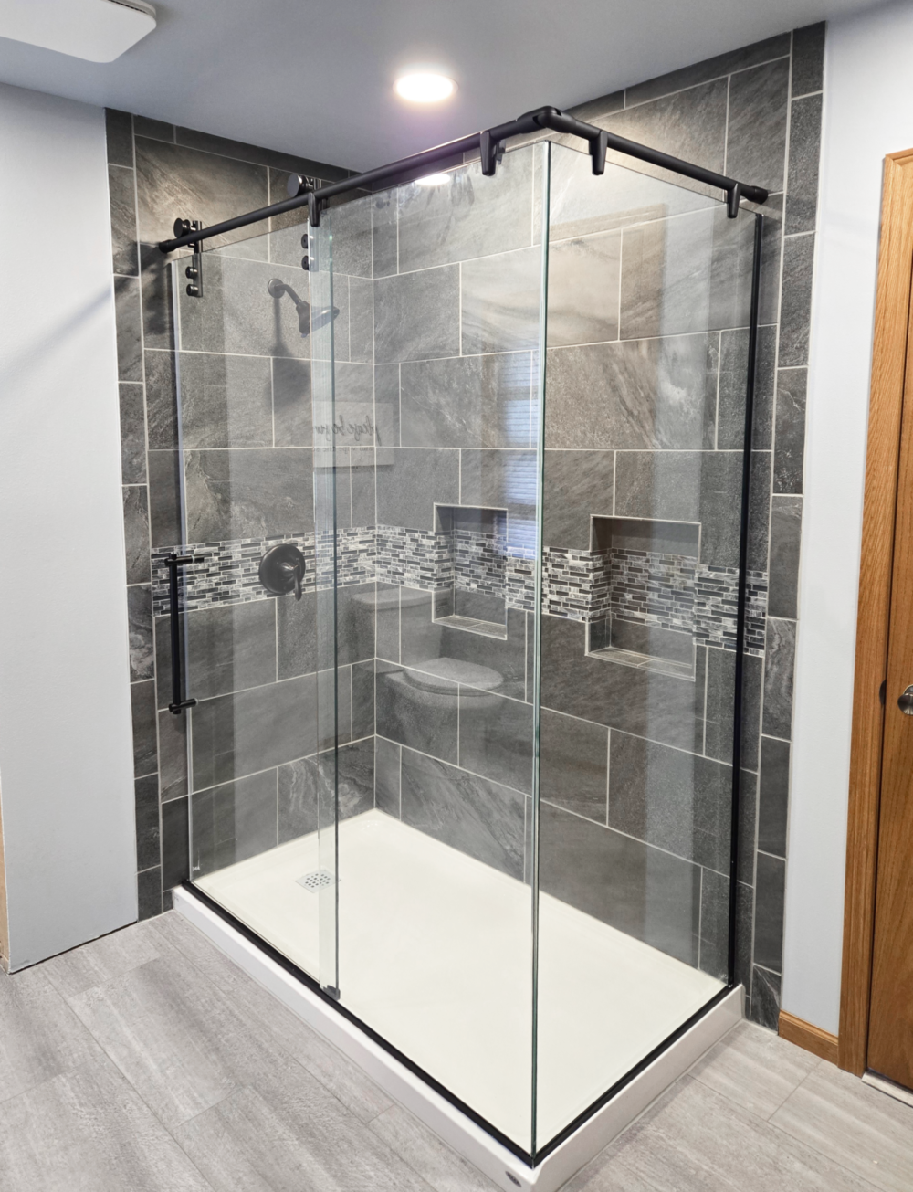 Rolaire 950 Shower enclosure featuring a rolling door panel, a fixed panel and return panel. The enclosure has Clear glass and a Matte Black metal finish.