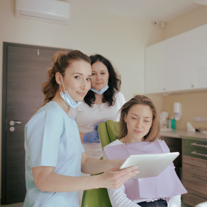 Dentist and assistant showing a patient something on a tablet in a dentist's office.