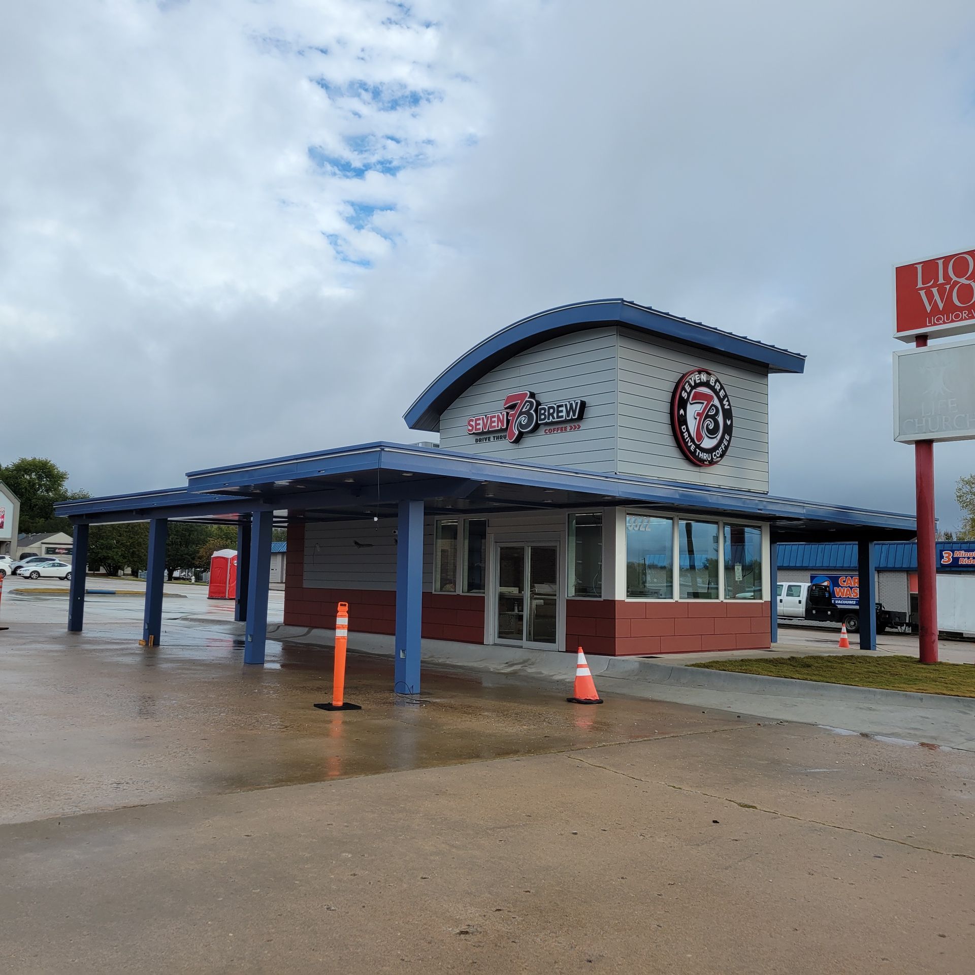 A modern, blue and grey restaurant building with a large covered drive-through area on a cloudy day.