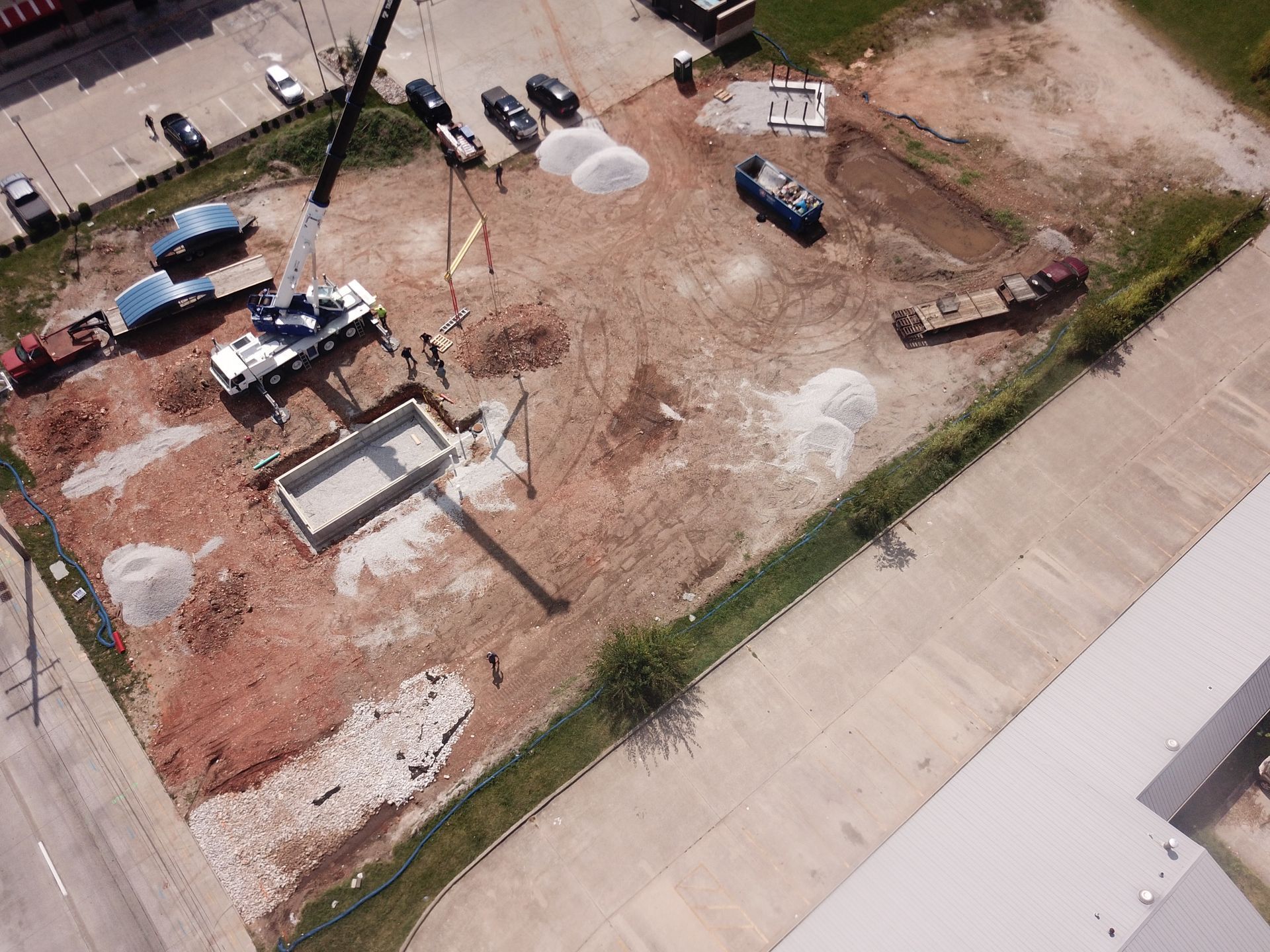 An aerial view of a construction site with a mobile crane lifting a precast concrete structure into place.