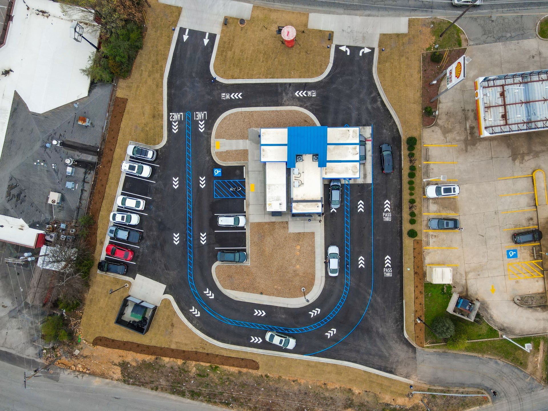 Aerial view of a car wash with dual lanes and parking spaces, surrounding a central building with a blue roof.