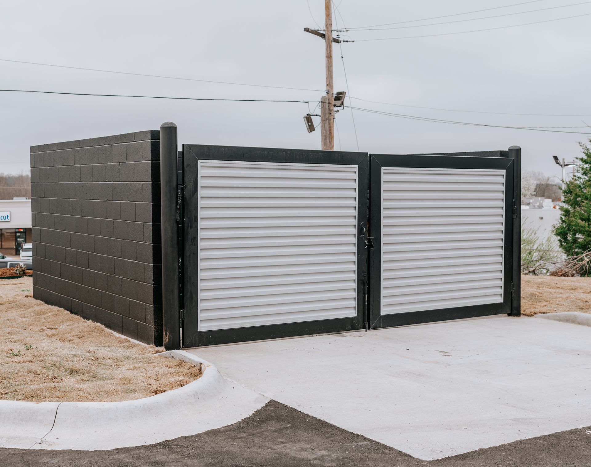 A black metal enclosure with silver corrugated metal gate panels, situated on a concrete pad outdoors.