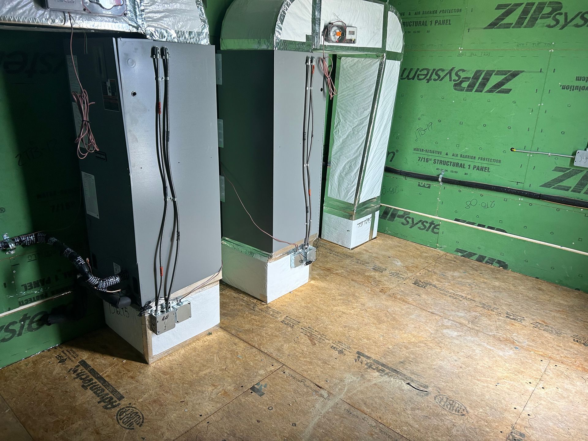 Two HVAC air handler units installed on a plywood floor against green ZIP System wall panels.