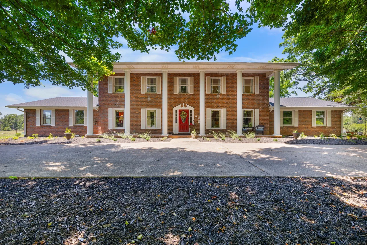 A large brick house with a driveway and trees in front of it.