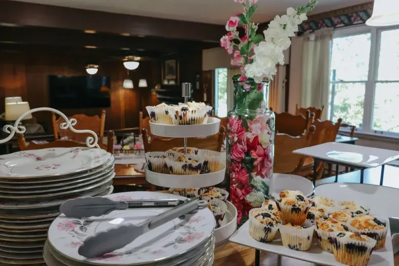 A table topped with plates , tongs , cupcakes and a vase of flowers.