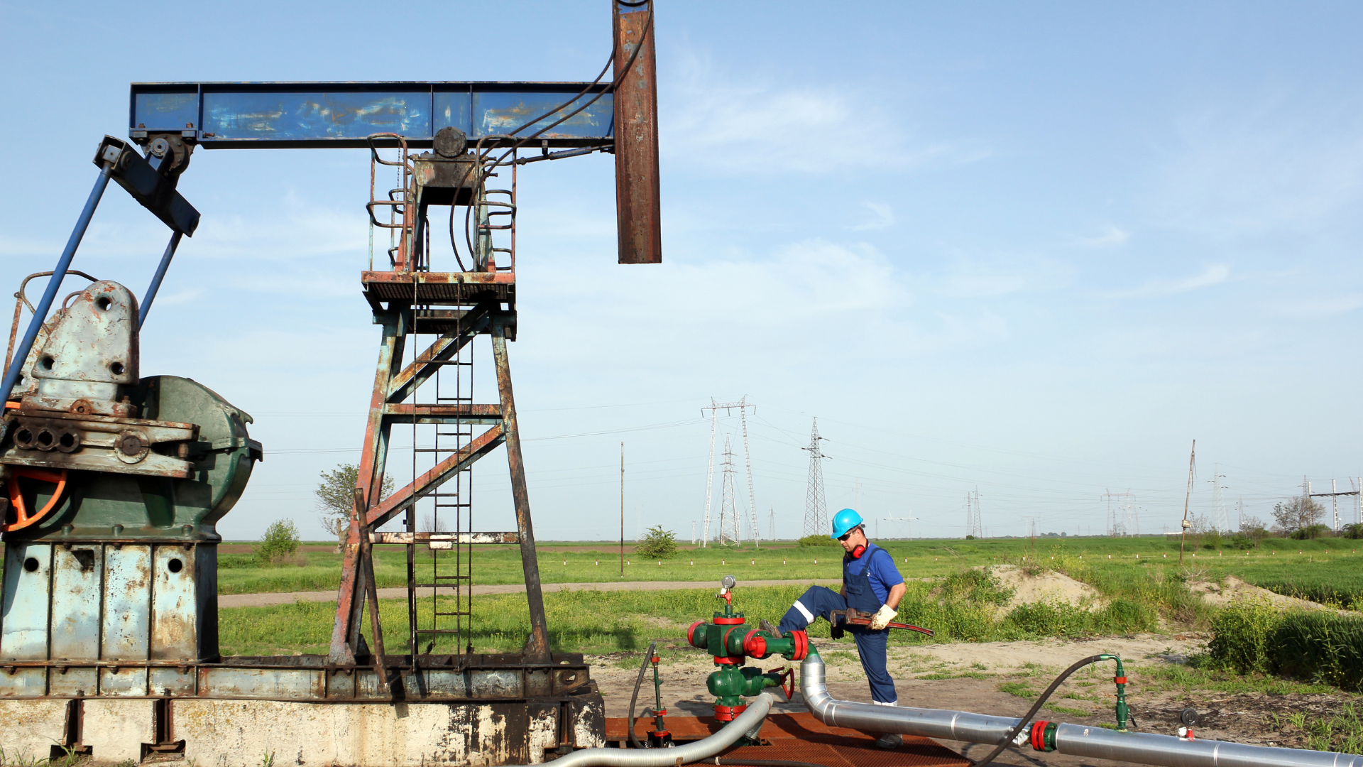 A man is standing in front of an oil pump in a field.