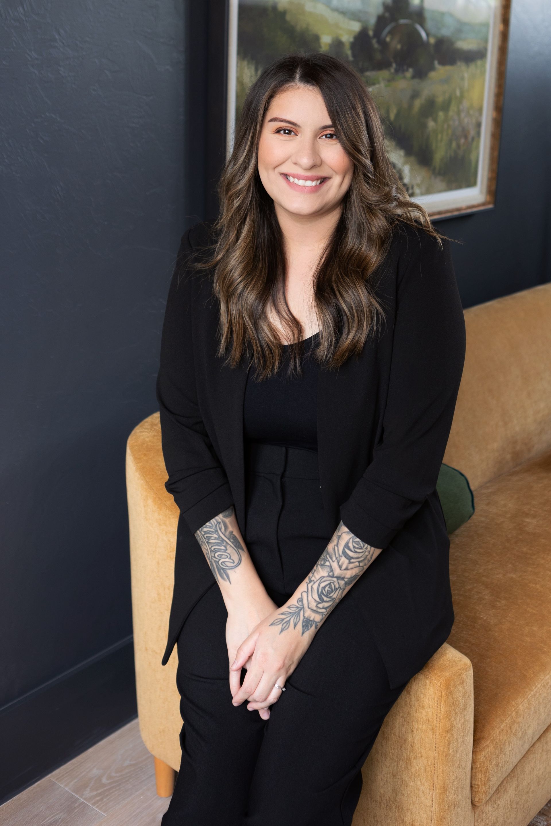 A woman is sitting at a desk with a laptop and a vase of flowers.
