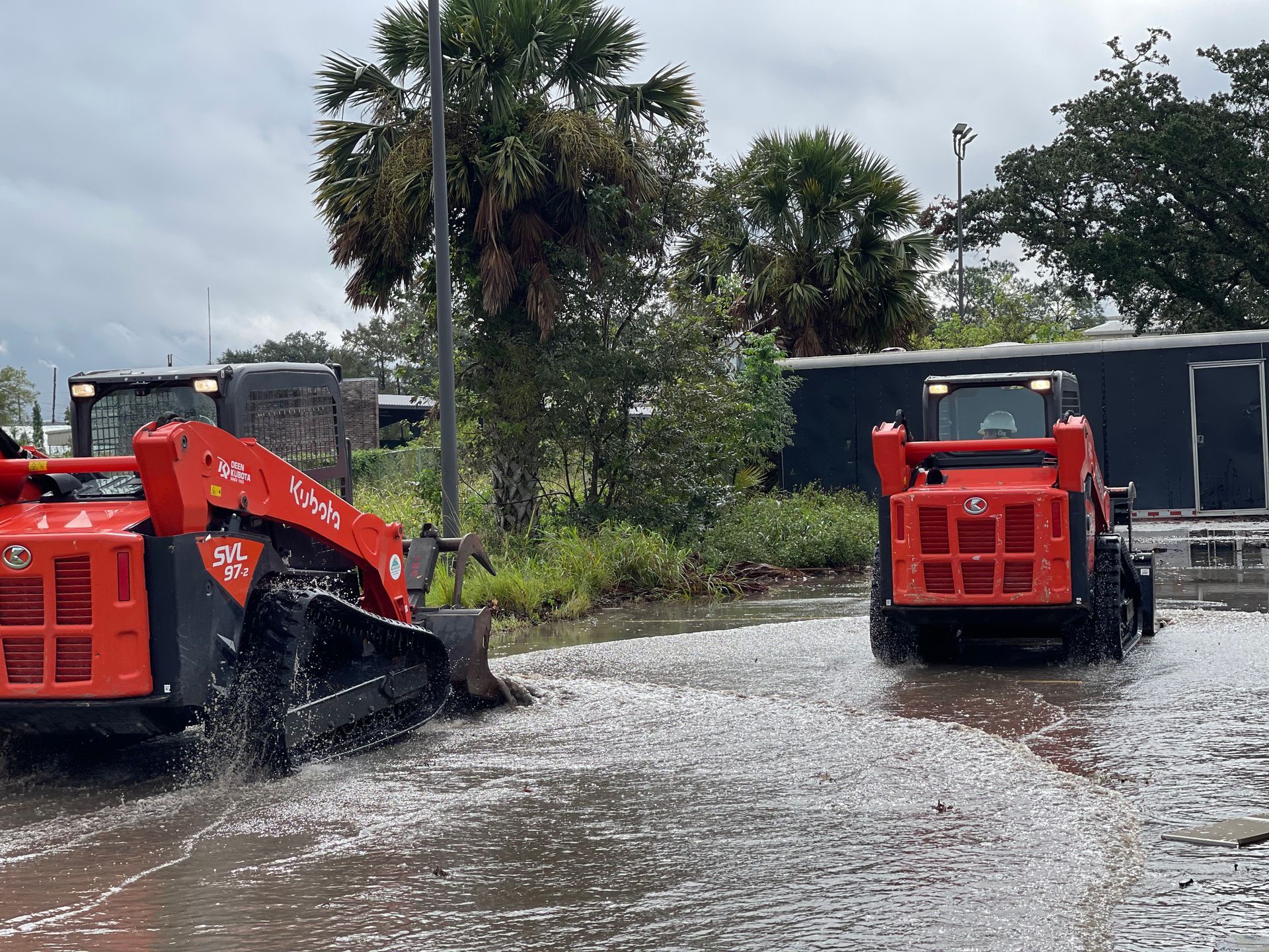 Two tractors are driving through a flooded street.