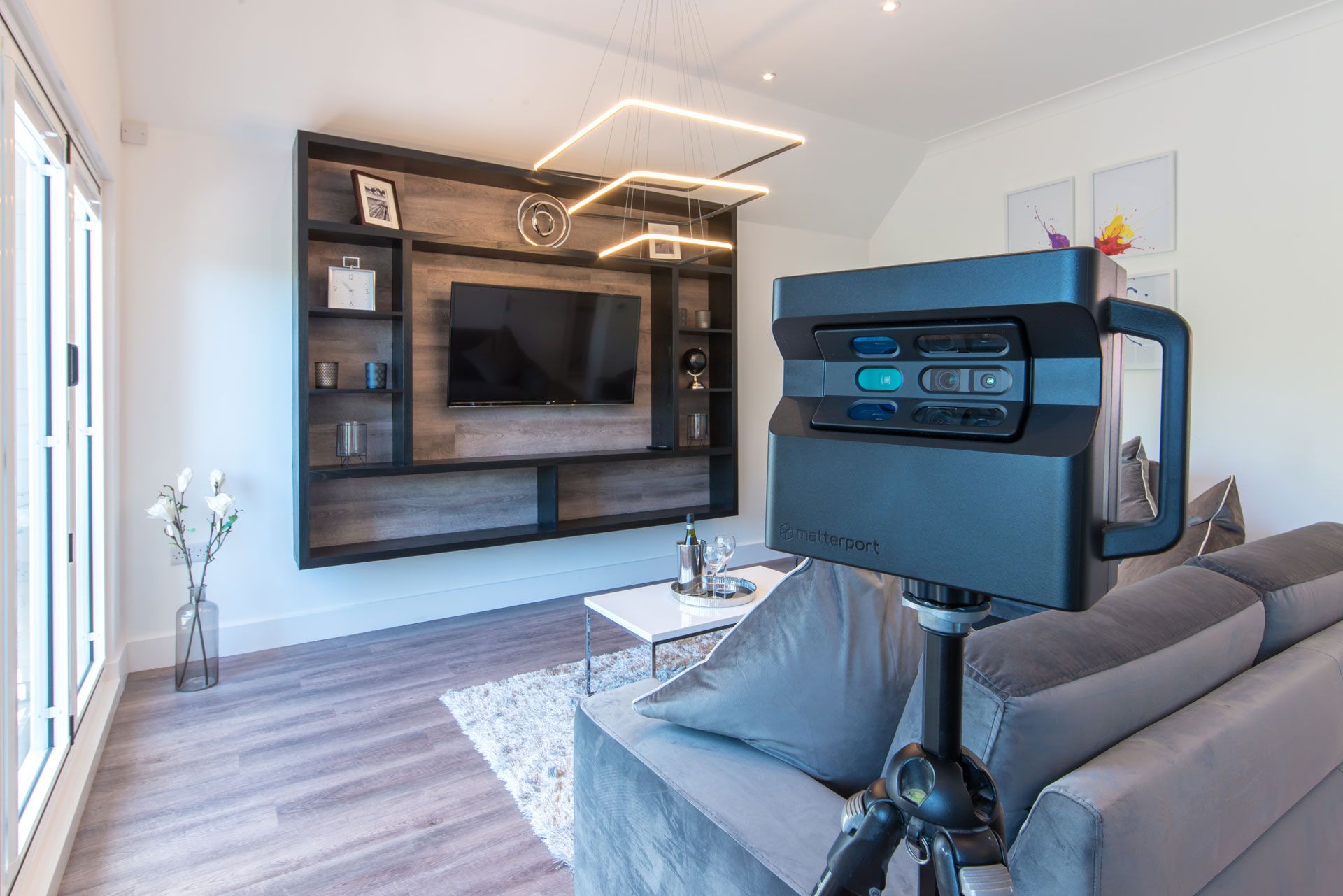 Modern living room with gray sofa, wall-mounted TV, built-in shelves, and geometric ceiling light