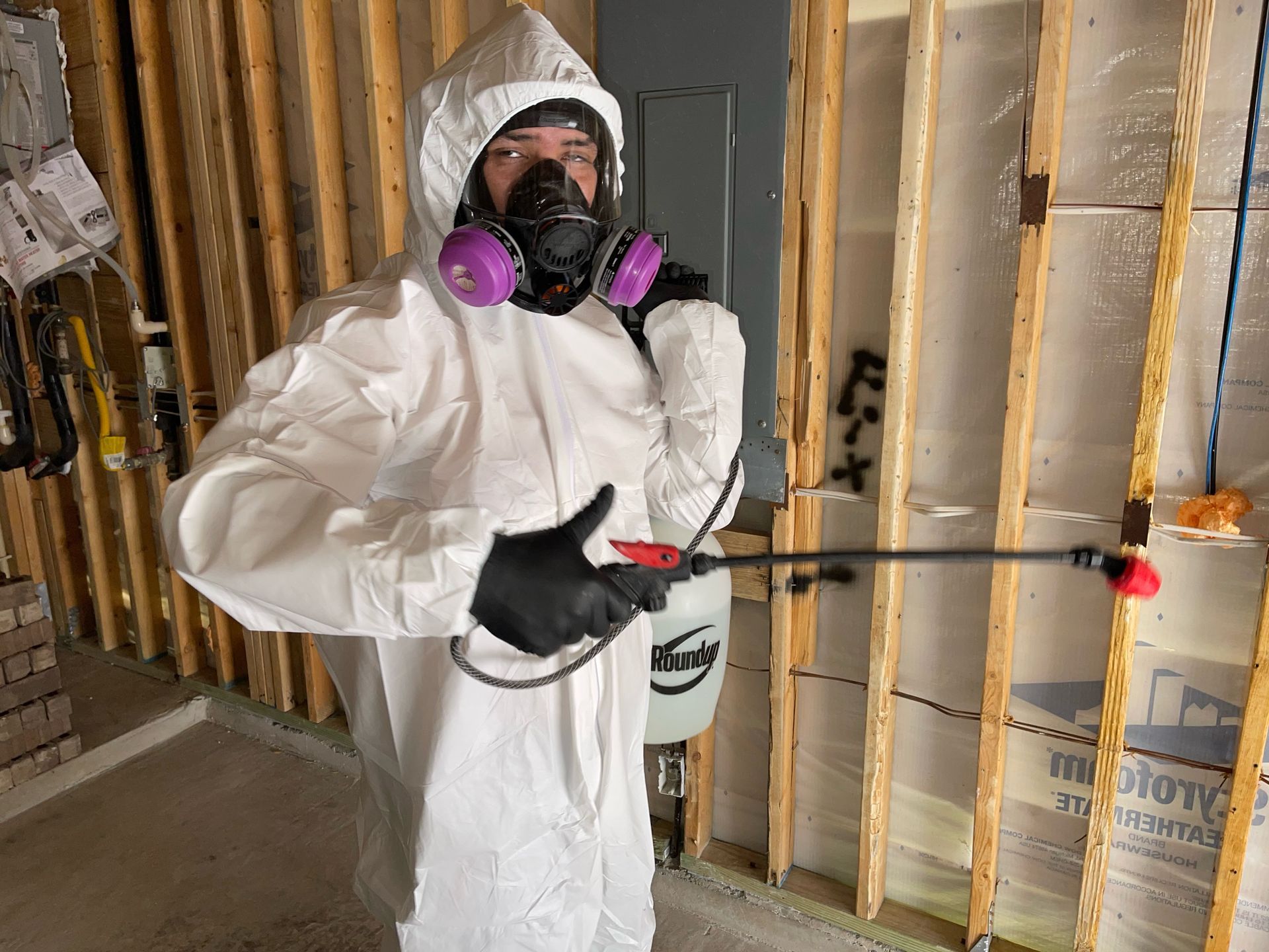 A man in a protective suit is spraying a wall with a sprayer.