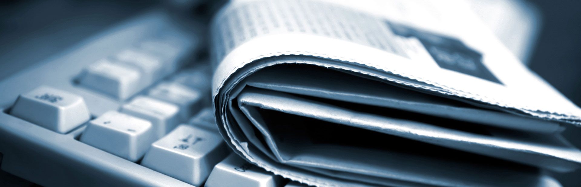 A newspaper is sitting on top of a computer keyboard
