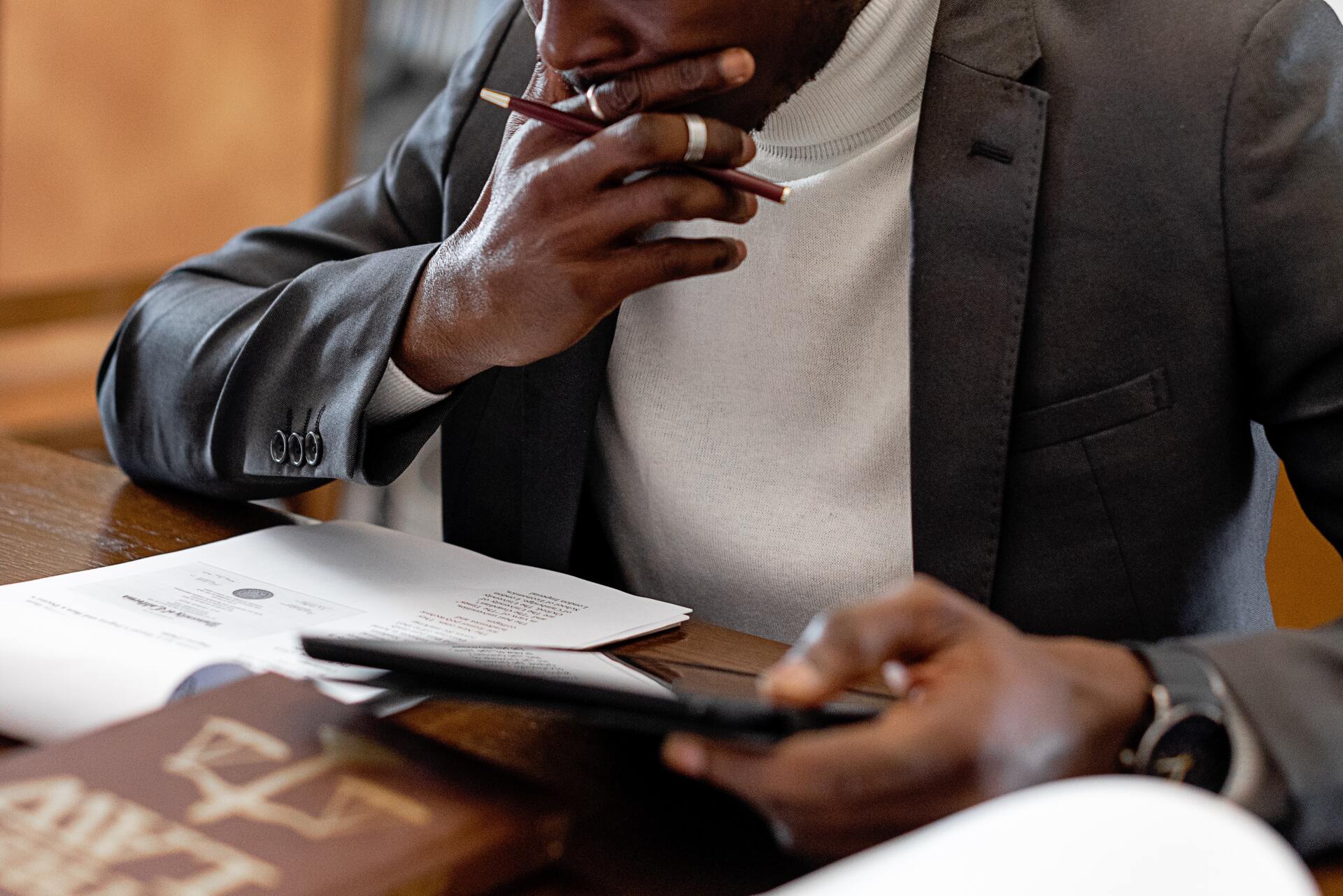 A man in a suit is sitting at a table with papers and a tablet.