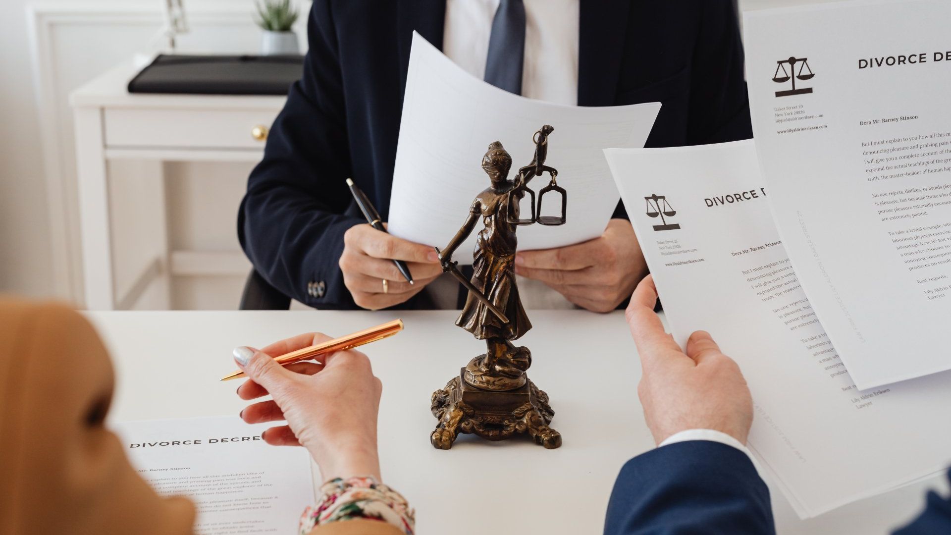 A group of people are sitting at a table with papers and a statue of justice.