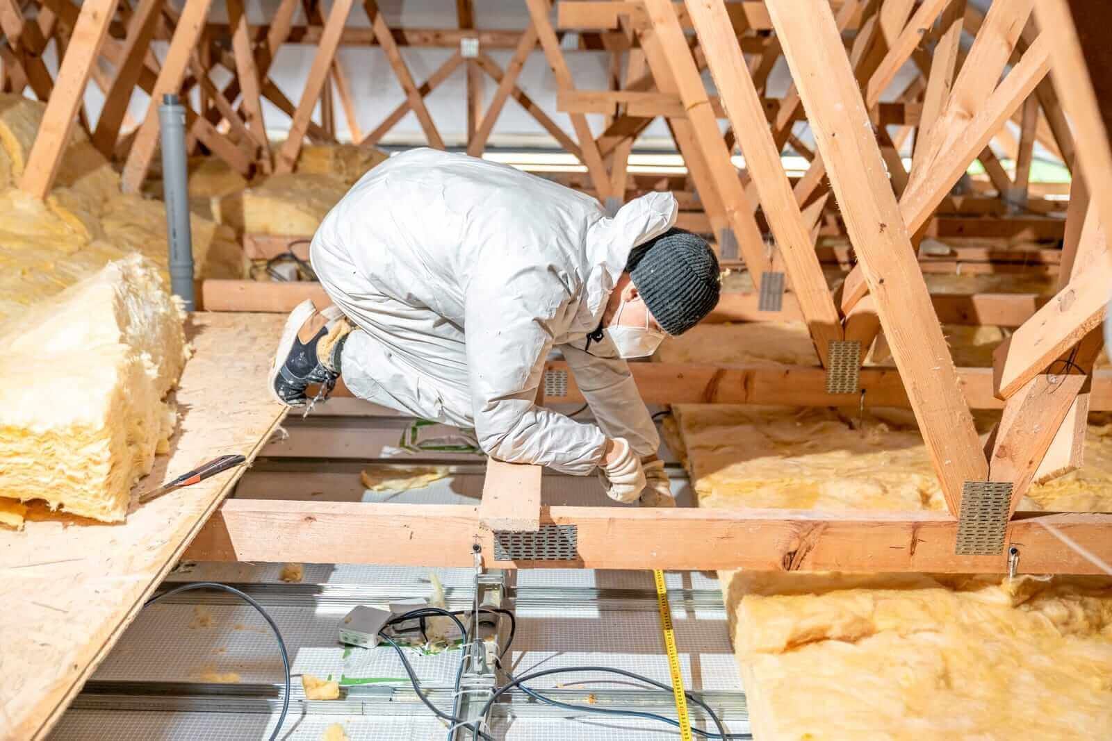 A man in overalls installing fiberglass insulation into an attic in Reno, NV