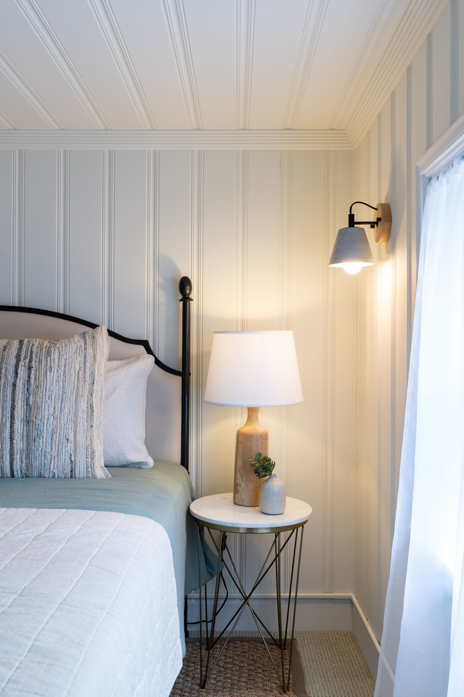 A bedroom with a bed , nightstand , lamp and window.