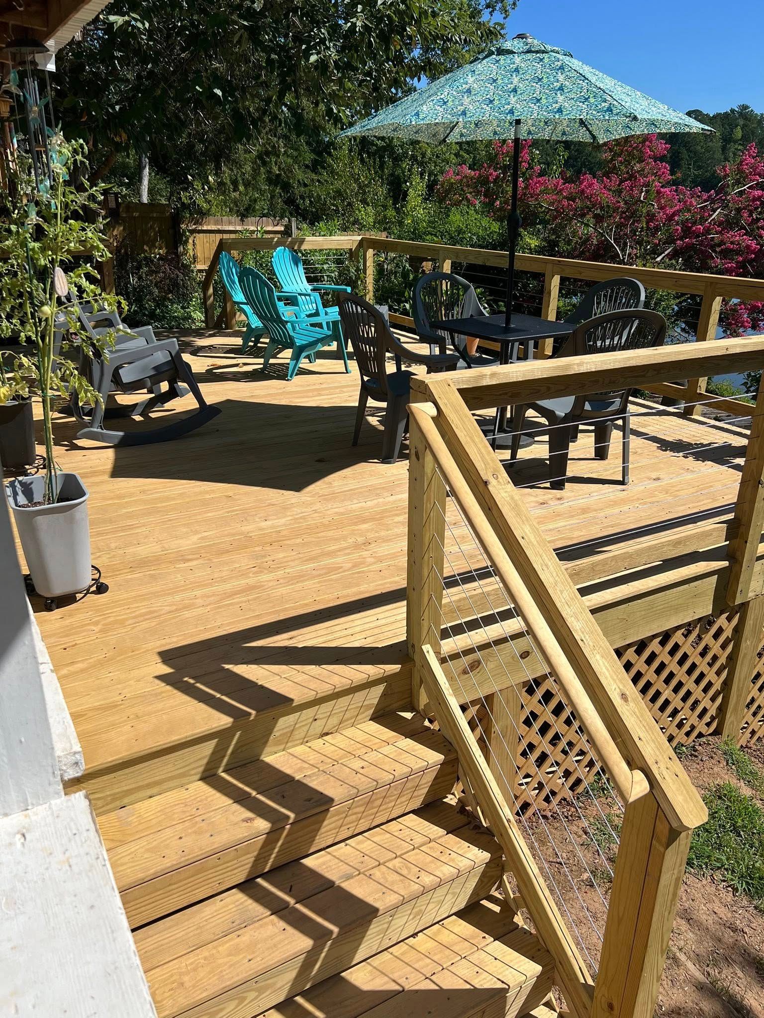 Wooden deck with stairs, seating, and a teal umbrella. Sunny outdoor setting.
