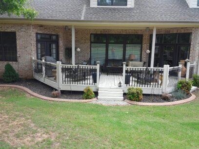 A large white deck with a black railing is in the backyard of a brick house.