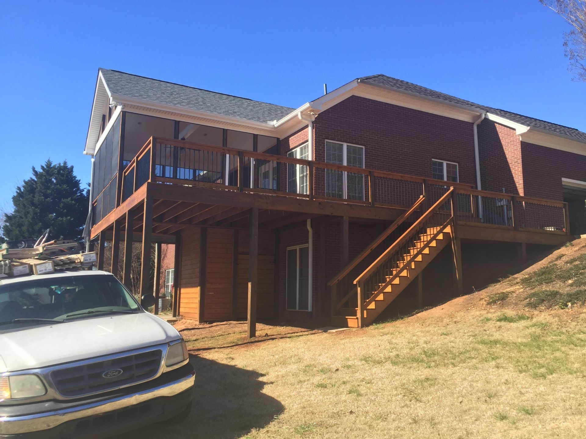 A white truck is parked in front of a house with a large deck.