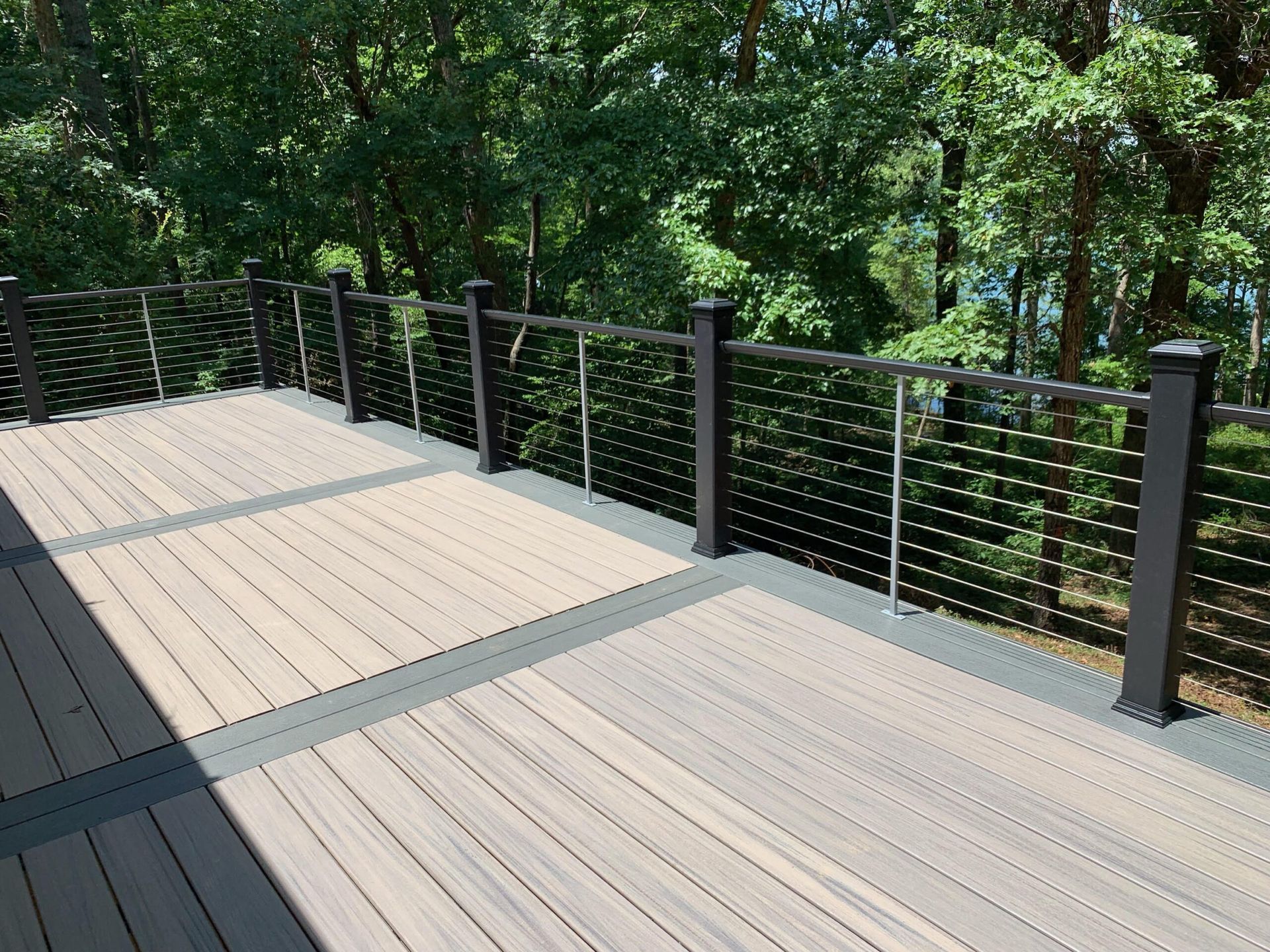 A wooden deck with a black railing and trees in the background.