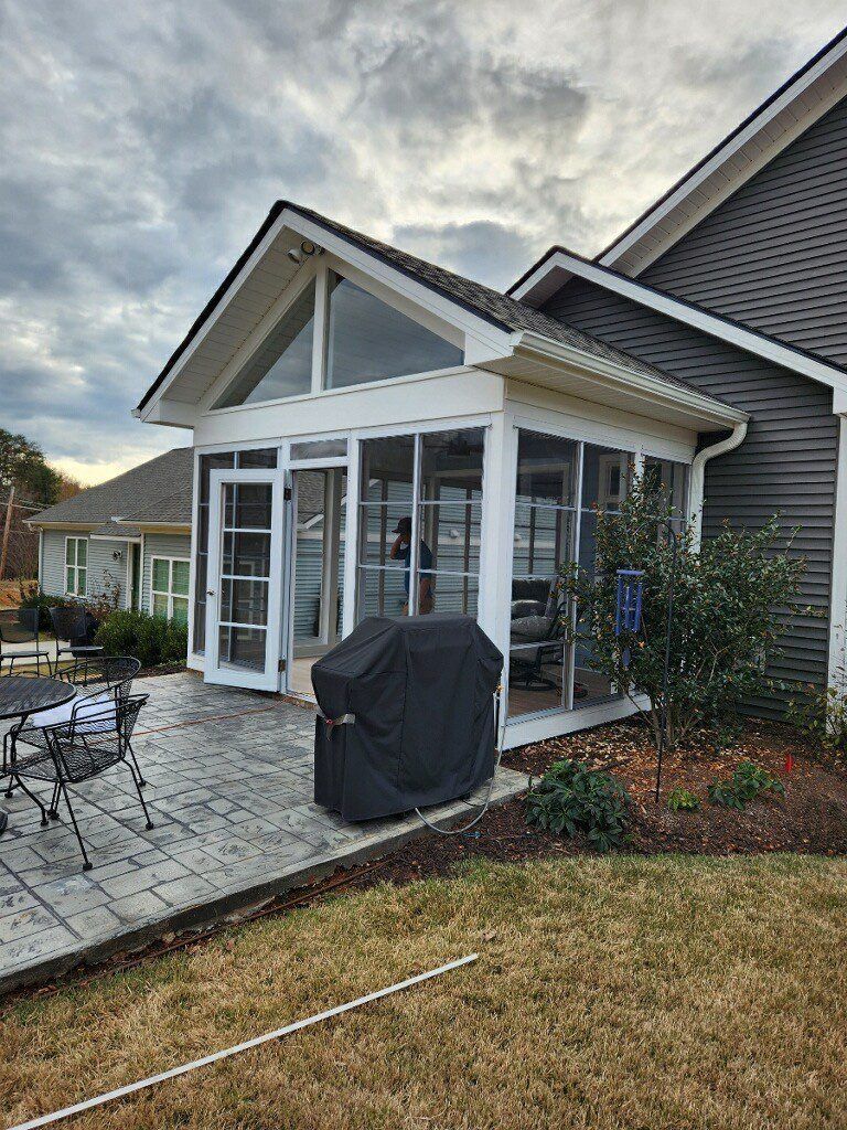 A house with a screened in porch and a grill in front of it.