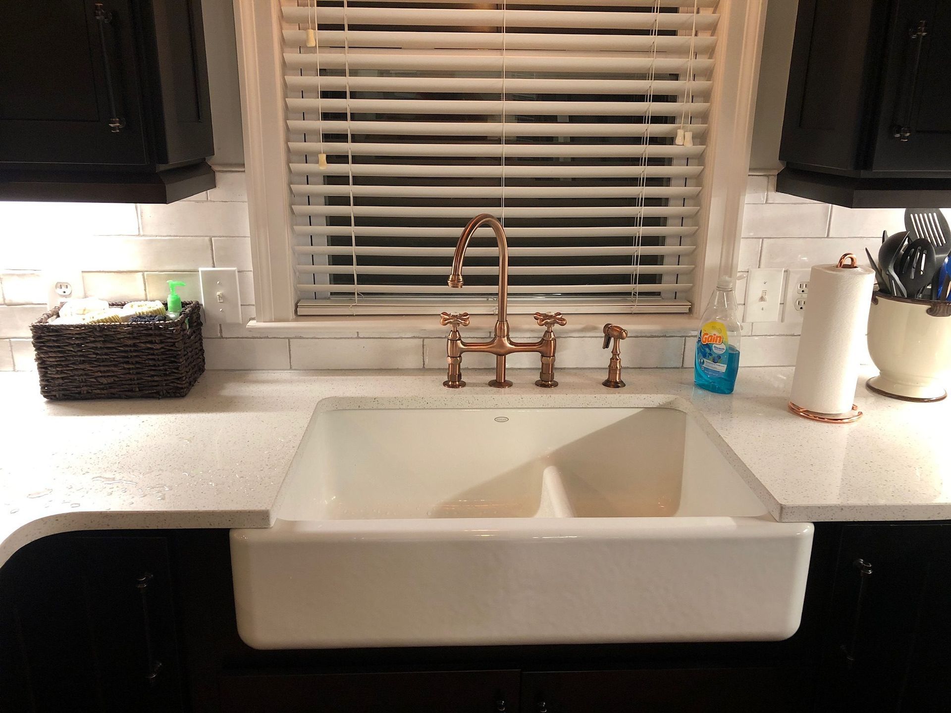 A kitchen sink with a copper faucet and a window with blinds.