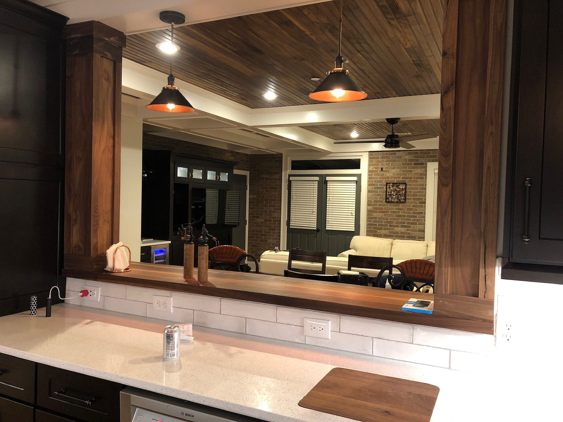 A kitchen with a large mirror over the counter and a view of a living room.