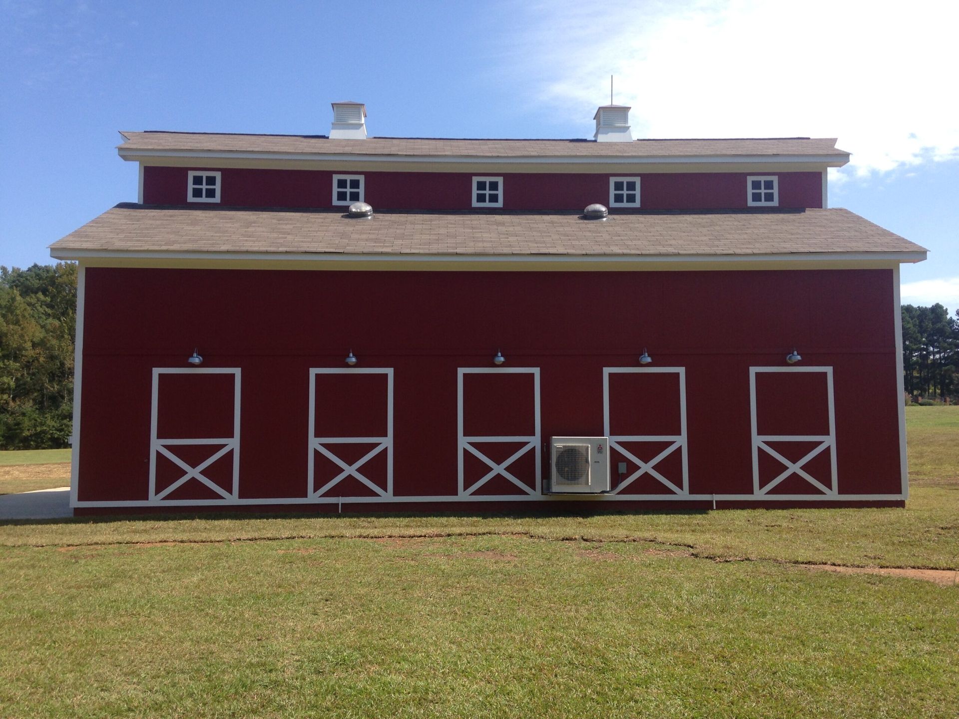 A red barn with four white doors is in a grassy field