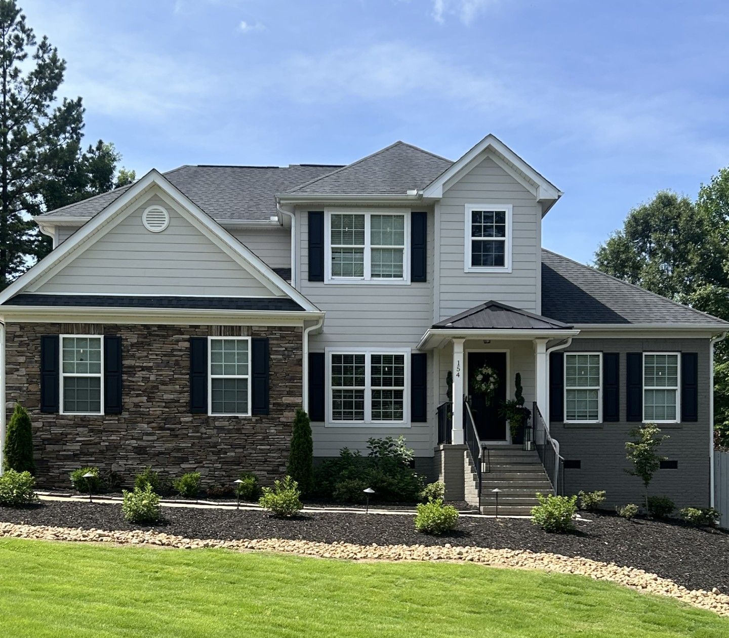 A large white house with black shutters and a stone facade
