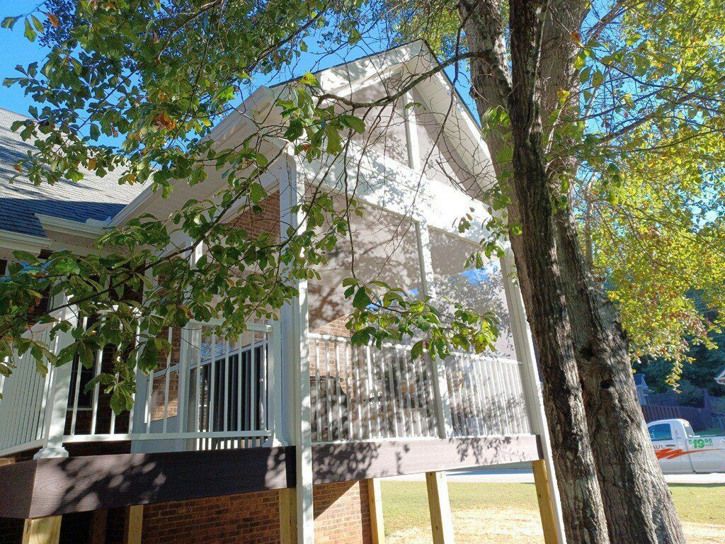 A white house with a porch and a tree in front of it.