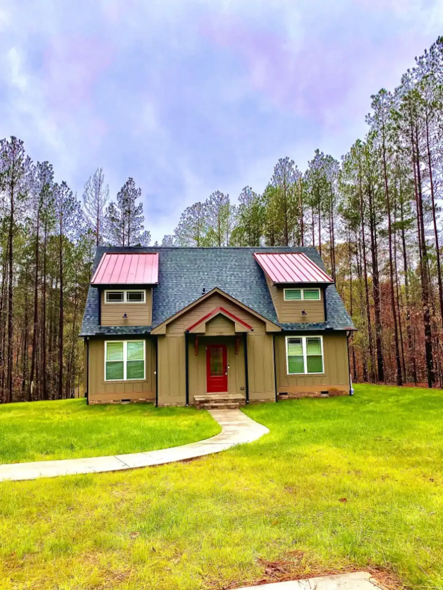 A house with a red door is in the middle of a lush green field surrounded by trees.