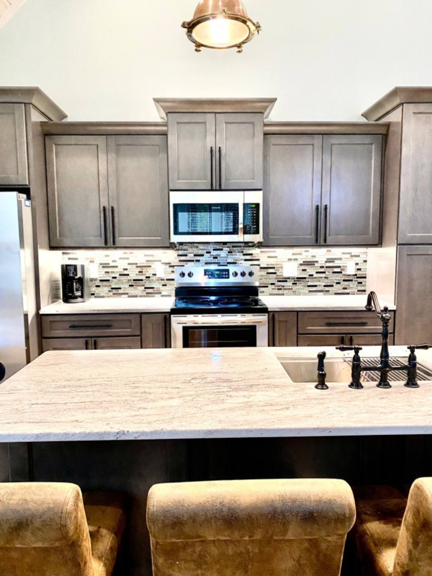 A kitchen with a stove , microwave , sink and chairs.