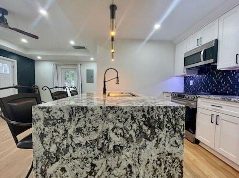 A kitchen with granite counter tops , white cabinets , stainless steel appliances and a large island.