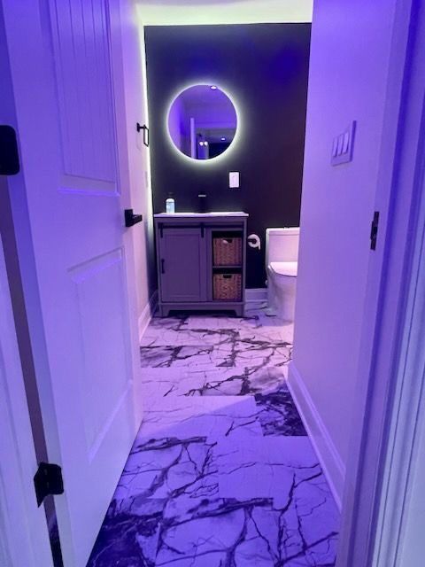 A bathroom with a sink , toilet , mirror and purple lights.