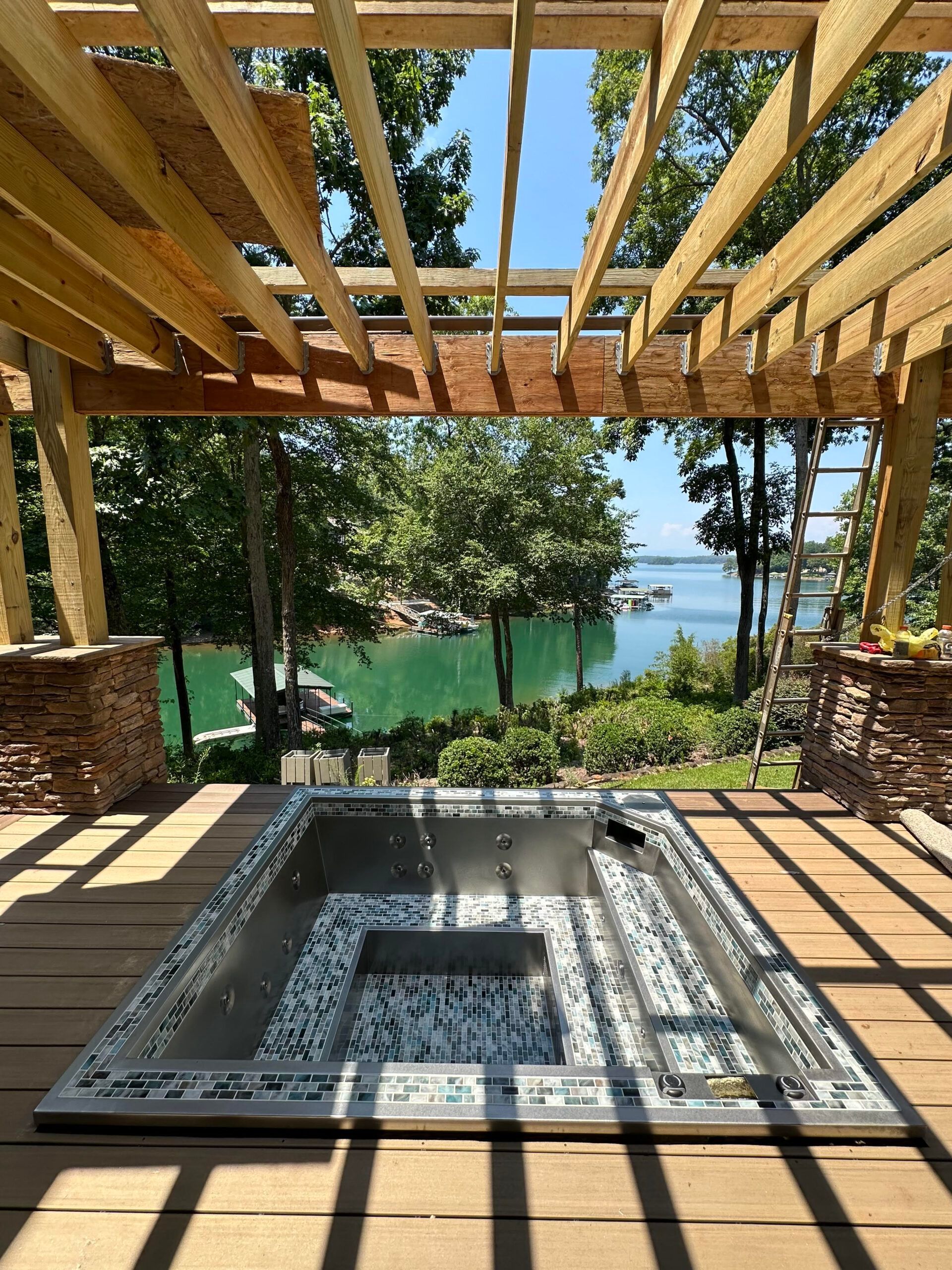 A hot tub is under a wooden pergola overlooking a lake.